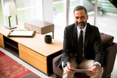 Ofiste çoklu görev multimedya dijital tableti kullanan yakışıklı, olgun bir iş adamı