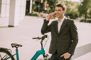 Bisikletli genç bir işadamı cep telefonu kullanıyor.
