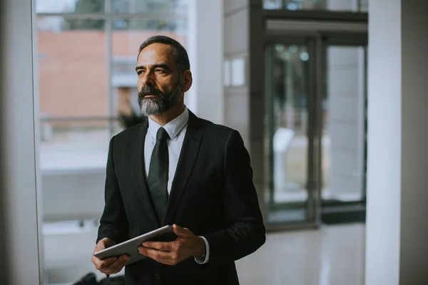 Handsome mature businessman standing in an office with digital tablet