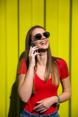 Sarı duvarın yanında cep telefonu kullanan güzel bir kadın.