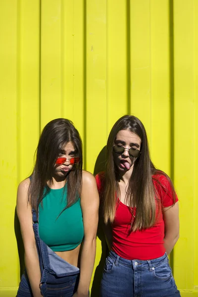 Две Милые Случайные Девушки Валяют Дурака Перед Желтой Стеной — стоковое фото