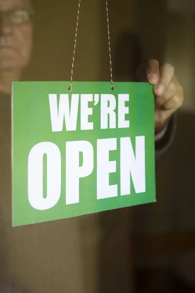 Closeup of the business owner hanging an open sign at a glass door