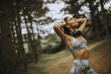 Ormanda koştuktan sonra müzik dinleyip ara veren genç ve çekici bir bayan koşucu.