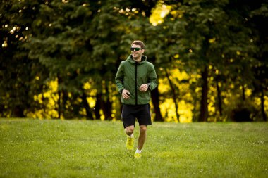 Atletik yakışıklı genç adam güneşli yeşil parkta çalışırken koşuyor.