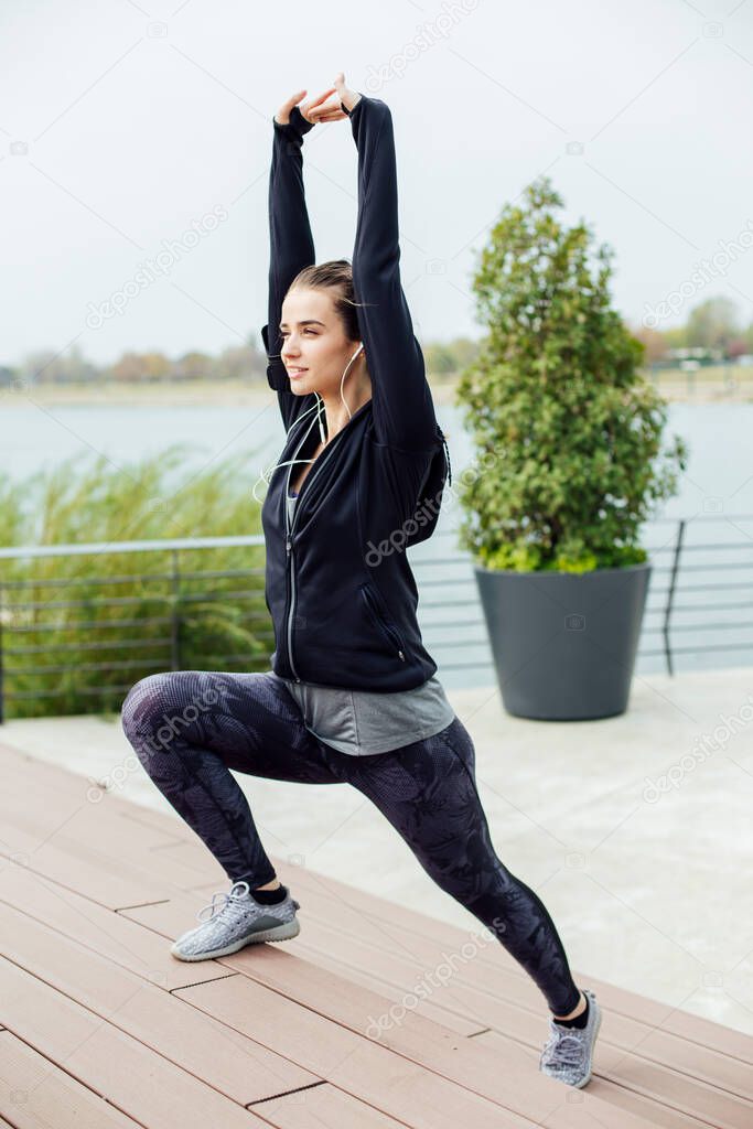 Fit young woman with earphones doing stretching exercises on urban stairs outdoors