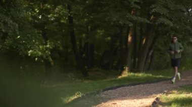 Atletik yakışıklı genç adam güneşli yeşil parkta çalışırken koşuyor.