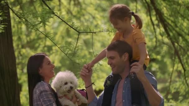 Linda família feliz está se divertindo com bichon cão ao ar livre no parque — Vídeo de Stock