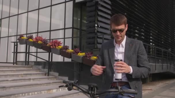 テイクアウトコーヒーカップと自転車の上にハンサムな若いビジネスマン — ストック動画