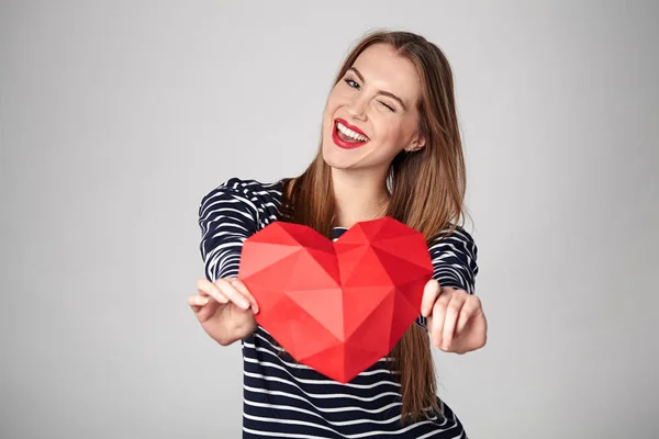 Donna sorridente che tiene la forma del cuore di carta poligonale rossa — Foto Stock