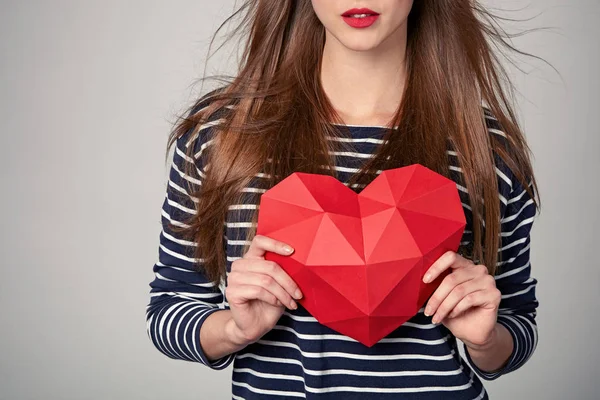 Donna sorridente che tiene la forma del cuore di carta poligonale rossa — Foto Stock