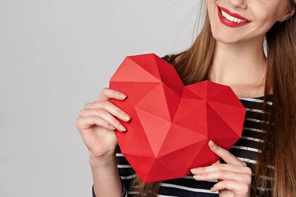 Mujer sonriente sosteniendo papel poligonal rojo en forma de corazón — Foto de Stock