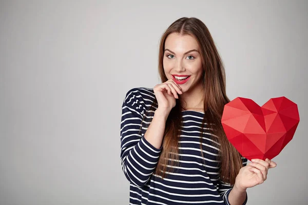 Mujer sonriente sosteniendo papel poligonal rojo en forma de corazón — Foto de Stock