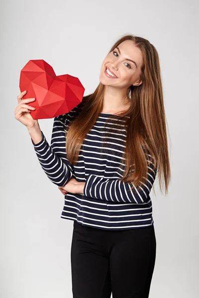 Mujer sonriente sosteniendo papel poligonal rojo en forma de corazón — Foto de Stock