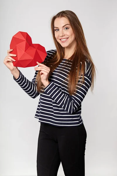 Mujer sonriente sosteniendo papel poligonal rojo en forma de corazón —  Fotos de Stock