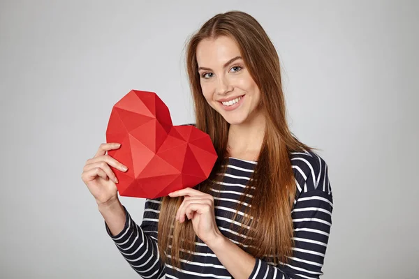 Donna sorridente che tiene la forma del cuore di carta poligonale rossa — Foto Stock