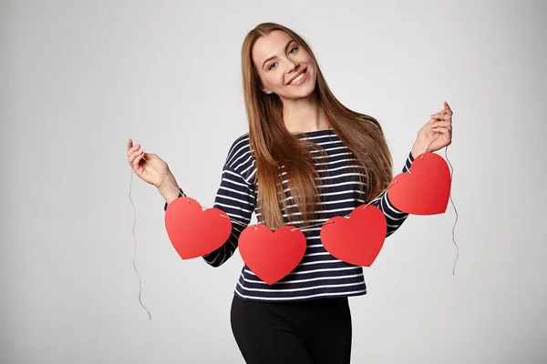 Mujer sonriente sosteniendo guirnalda de cinco corazones de papel rojo — Foto de Stock