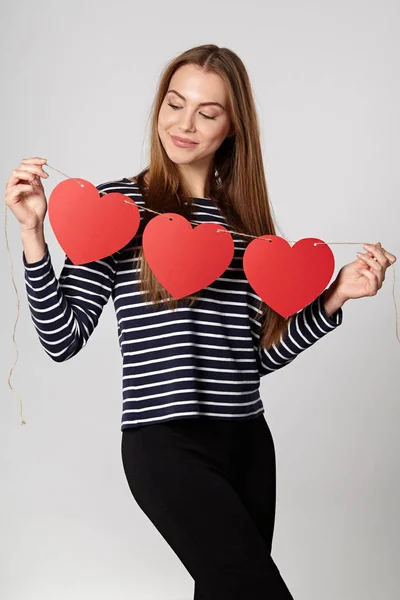 Mujer sonriente sosteniendo guirnalda de tres corazones de papel rojo —  Fotos de Stock