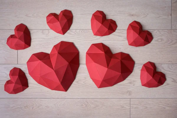 Banyak kertas poligonal merah berbentuk hati di atas tanah lapang kayu — Stok Foto