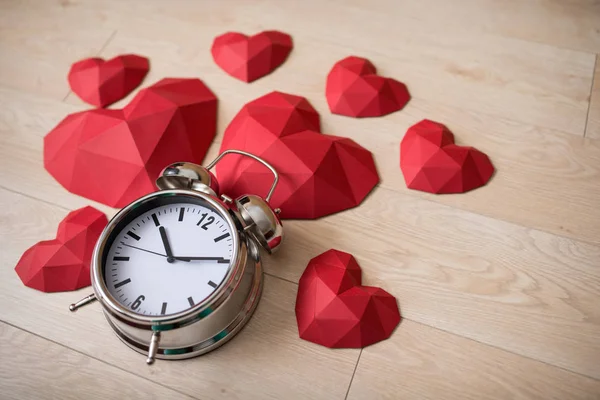 Penutupan jam alarm besar dengan banyak bentuk kertas poligonal merah jantung — Stok Foto