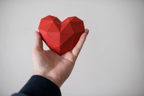 Mano maschile tenendo forma di cuore poligonale rosso — Foto Stock