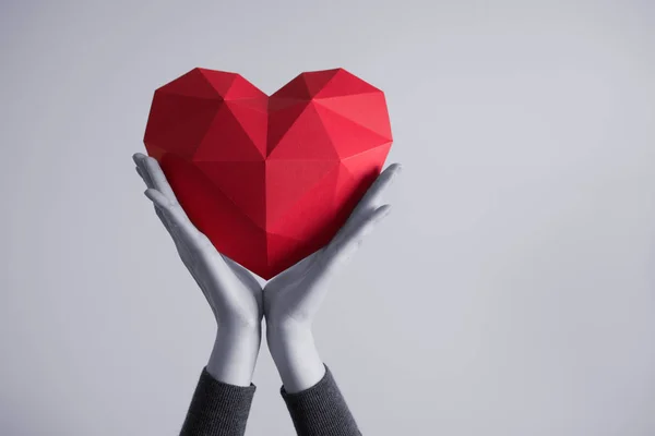 Mani femminili che tengono la forma del cuore poligonale rosso — Foto Stock