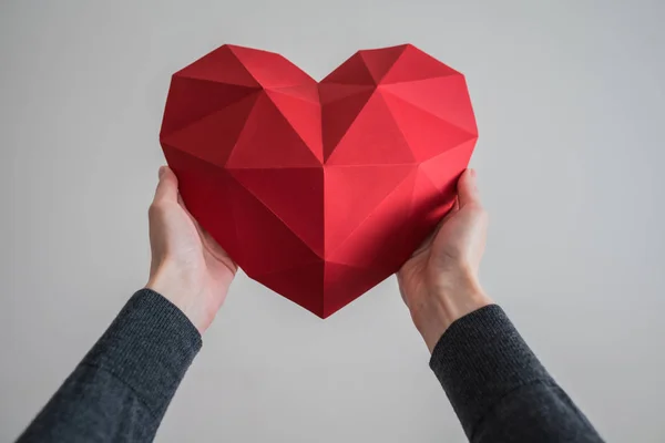 Tangan wanita memegang bentuk jantung poligonal merah — Stok Foto
