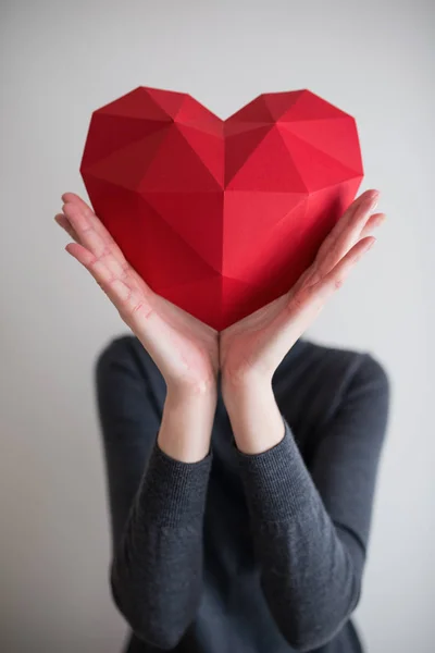 Femme montrant une forme de coeur en papier polygonal rouge — Photo