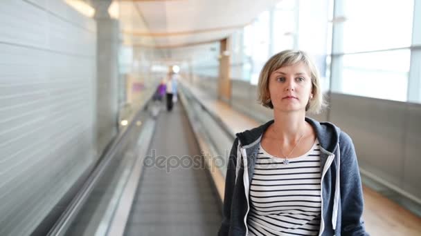 Frau steht auf fahrendem Gehweg im Flughafen — Stockvideo