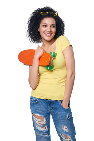 Feliz sonriente mezcla de raza femenina en pantalones vaqueros angustiados con monopatín — Foto de Stock