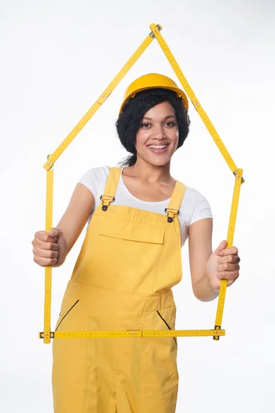 Женщина-строитель в желтом защитном шлеме и в целом показывает каркас дома — стоковое фото