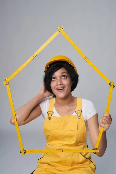 Mulher construtor vestindo amarelo proteger capacete e geral segurando casa quadro — Fotografia de Stock