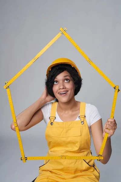 Жінка-будівельник носить жовтий захисний шолом і загальну рамку для будинку Стокове Фото
