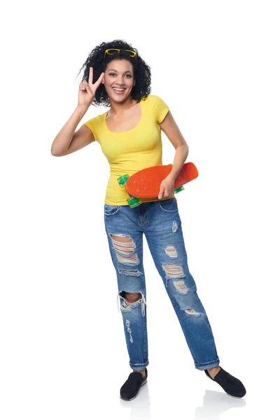 Mulher feliz em jeans angustiados com skate apontando para o lado — Fotografia de Stock