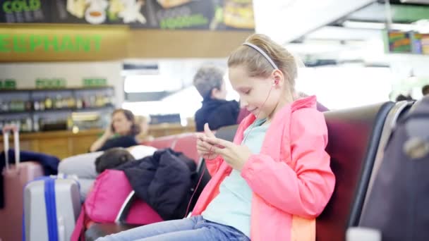 공항 홀에 스마트폰 게임을 재생 하는 어린 소녀 — 비디오