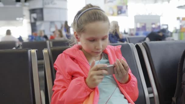 Liten flicka spela spel på smartphone i flygplats hall — Stockvideo