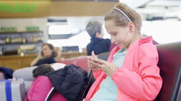 Liten flicka spela spel på smartphone i flygplats hall — Stockvideo