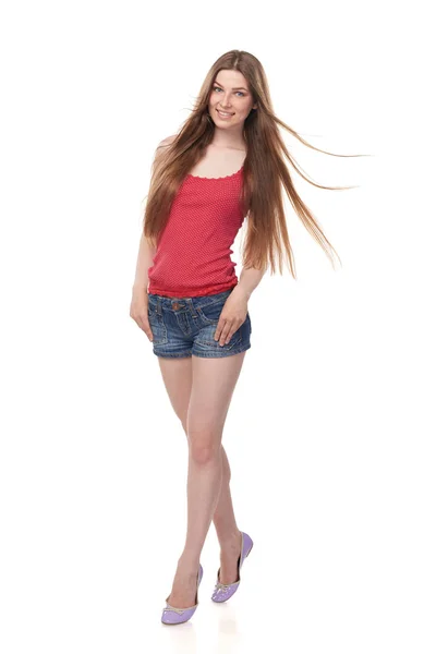 Улыбающаяся длинноногая молодая женщина в джинсовых шортах и красном топе с красивыми длинными волосами — стоковое фото