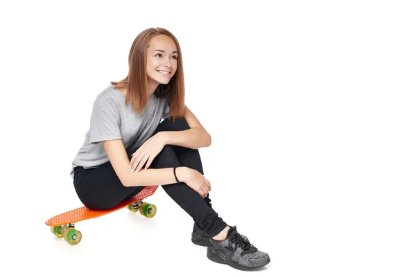 Teen girl in full length sitting on skate board — Stock Photo, Image