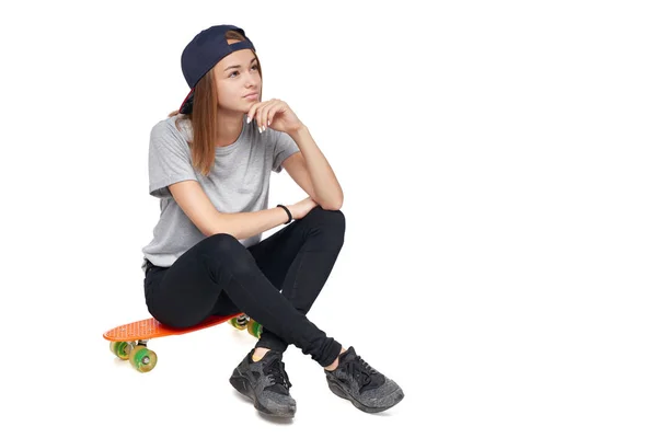 Дівчина сидить на скейтборді думаючи, дивлячись на бік — стокове фото