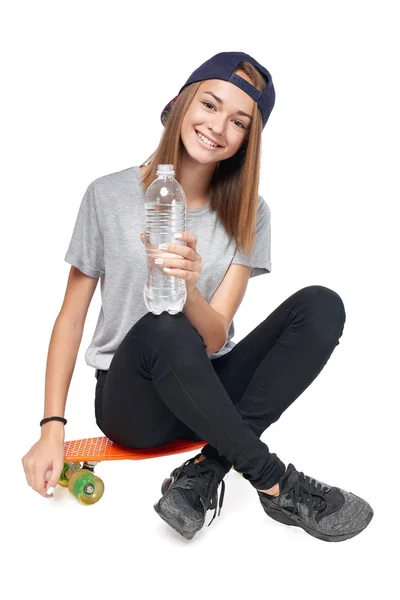 Chica adolescente sentada en patineta con botella de agua — Foto de Stock