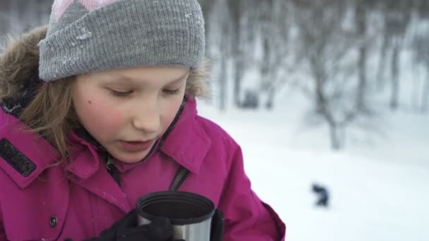 Маленькая девочка пьет горячий напиток на открытом воздухе зимой — стоковое видео