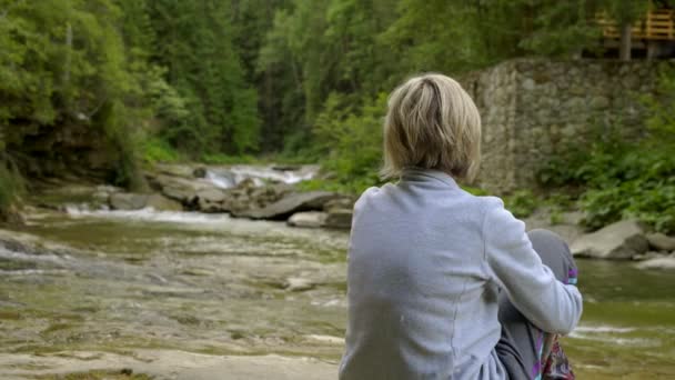 Жінка і маленька дівчинка сидять на скелях на гірській річці — стокове відео