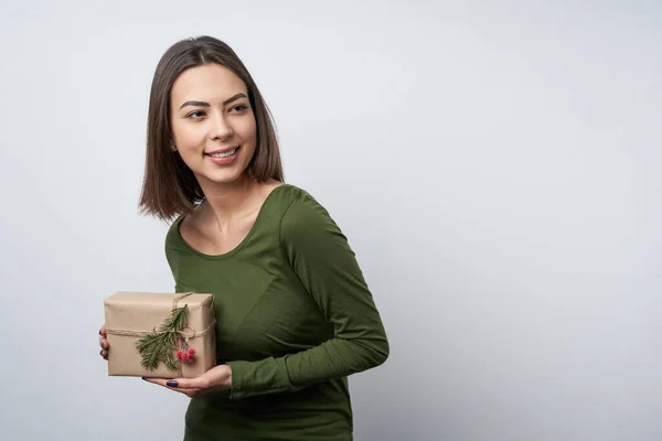 Happy girl holding a gift box wrapped in craft paper with a branch of fir tree — Stock Photo, Image