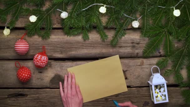 给圣诞老人的信 女人的手拿着一封信 放在一个用绿色的枞树枝干做成的框架上 上面的礼品盒放在粗糙的风吹日晒的木板上 平躺在地板上 — 图库视频影像