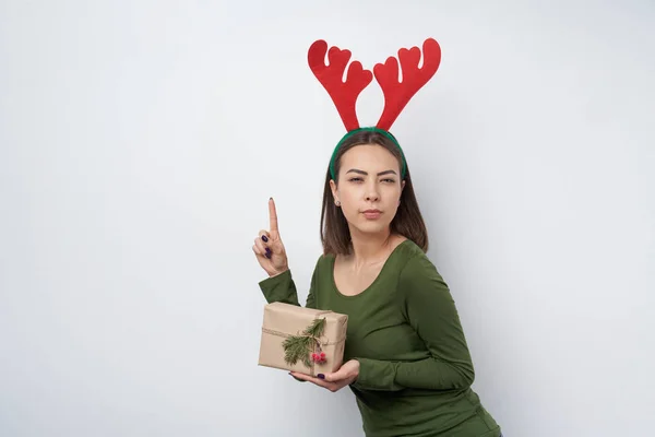 Lycklig flicka bär julrådjur horn hålla en presentförpackning pekar finger upp — Stockfoto