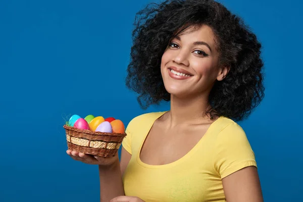 Lächelnde Frau mit einem Korb mit bunten Ostereiern — Stockfoto