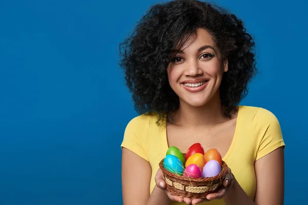 Усміхнена жінка тримає кошик з барвистими великодніми яйцями — стокове фото