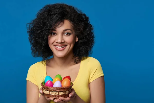 Χαμογελαστή γυναίκα κρατώντας ένα καλάθι με πολύχρωμα πασχαλινά αυγά — Φωτογραφία Αρχείου