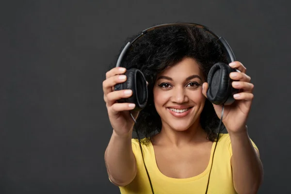 Mulher sorridente dando-lhe fones de ouvido, tiro estúdio — Fotografia de Stock