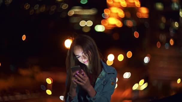 美しいですティーン女の子オン夜の街並みの背景とともに街路灯Bokeh保持携帯電話で手チャット — ストック動画